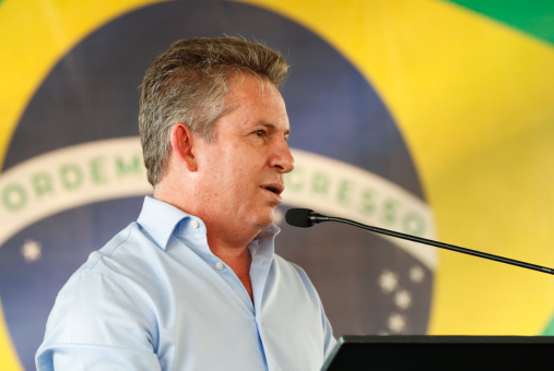 Photo of a middle aged man wearing a blue shirt against the national flag of Brazil