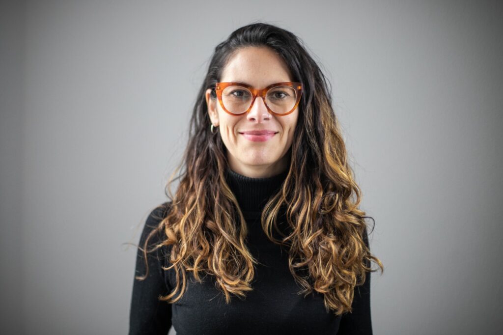 woman with long wavy hair and glasses posing to the camera